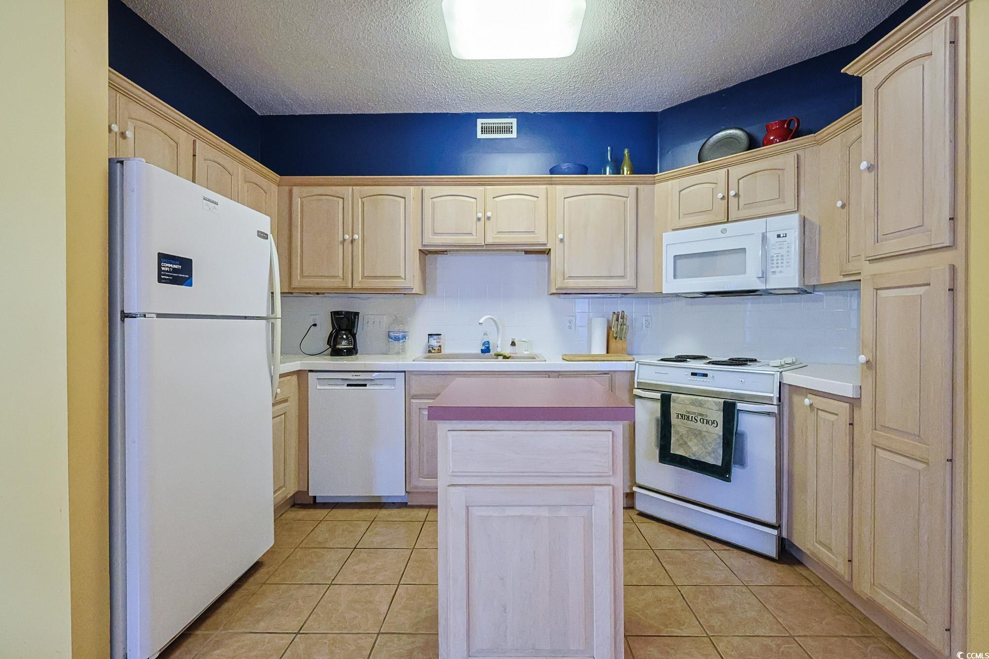2302 Sweetwater Boulevard, Unit 2302 Murrells Inlet, SC 29576 - Photo 9 of 24 Kitchen featuring light brown cabinetry, light countertops, light tile patterned floors, a textured ceiling, and white appliances