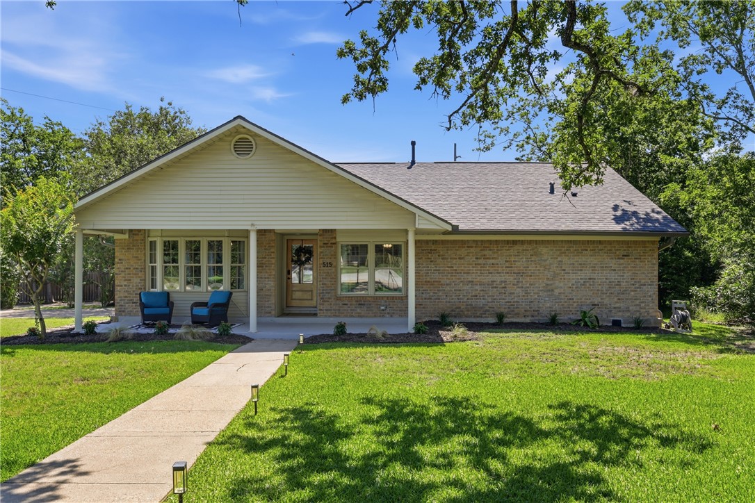 515 Crescent Drive Bryan, TX 77801 - Photo 1 of 43 Brick facade residence featuring a covered front porch, gabled roofline, multiple windows, a concrete walkway with integrated lighting, and mature trees
