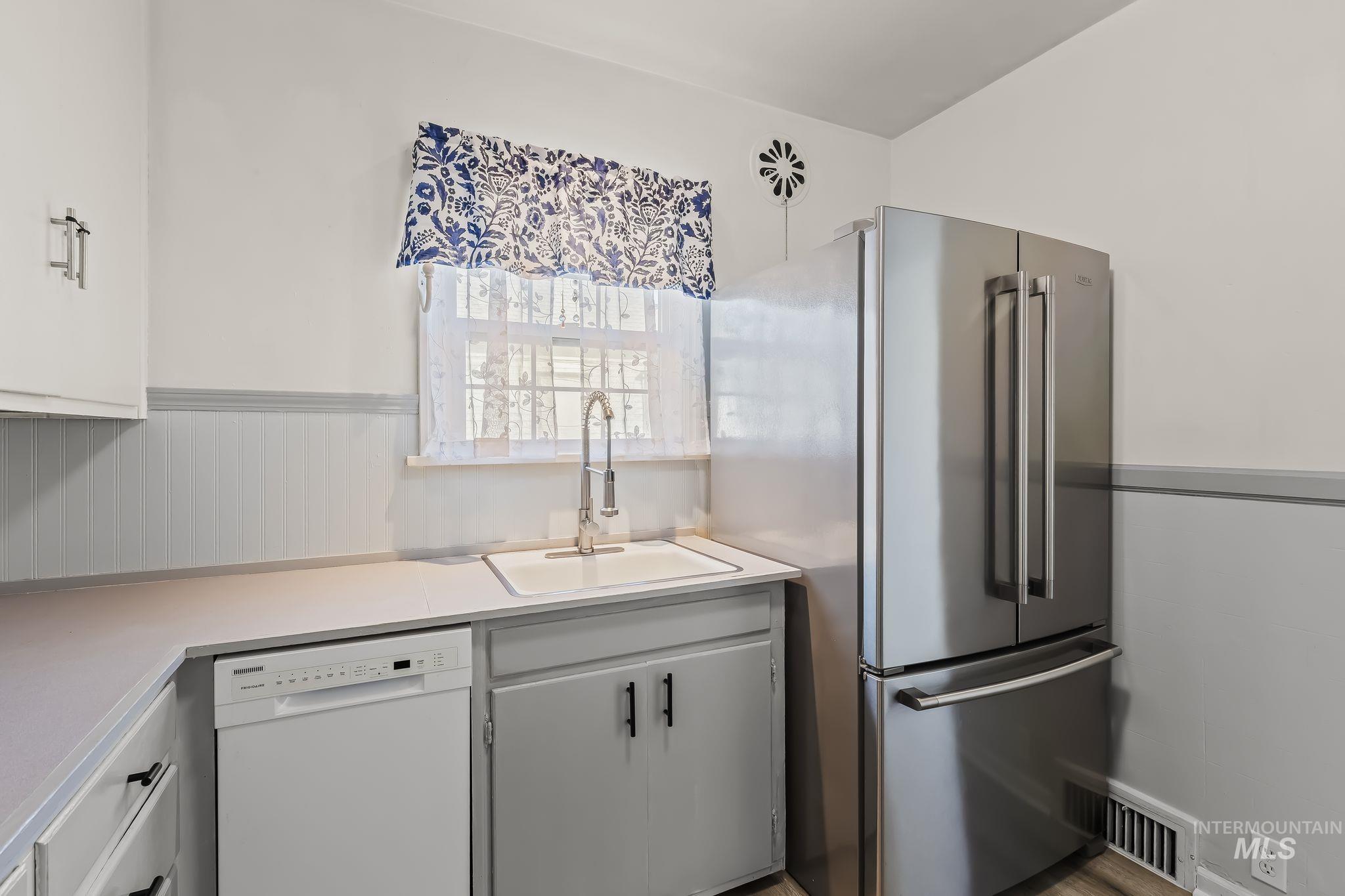 420 4th Street Lewiston, ID 83501 - Photo 17 of 38 Stainless steel refrigerator, white single-basin sink with a gooseneck faucet, white dishwasher, gray lower cabinetry with black hardware, and white upper cabinetry