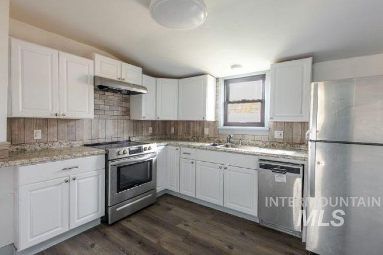 622 West Commercial Street Weiser, ID 83672 - Photo 12 of 21 Kitchen with stainless steel appliances, white cabinets, dark wood-type flooring, under cabinet range hood, and decorative backsplash