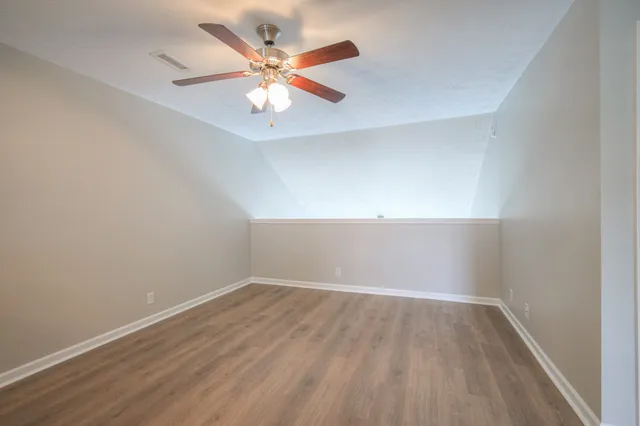 a view of an empty room with wooden floor and a ceiling fan