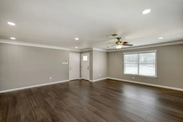 an empty room with wooden floor chandelier fan and windows