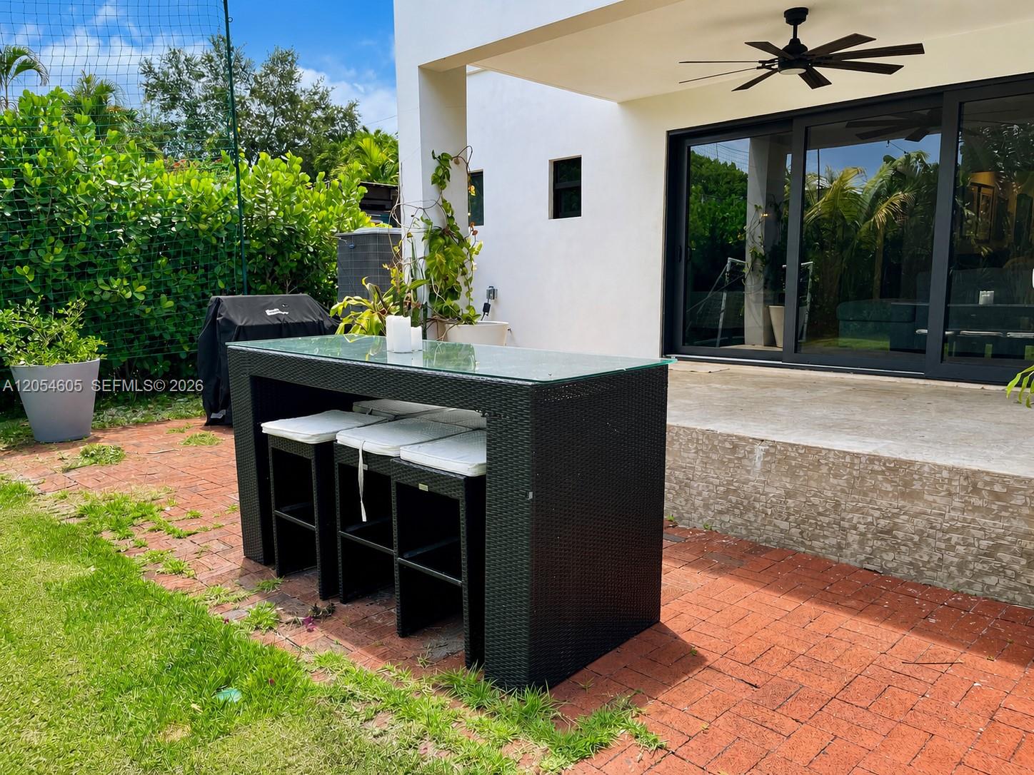 3538 Southwest 1st Avenue, Unit 1 Miami, FL 33145 - Photo 20 of 20 Versatile outdoor entertaining area featuring a covered patio with a ceiling fan, large sliding glass doors, and a bar-height dining table with seating. The adjoining brick patio includes space for grilling and connects directly to the lawn, creating a practical setting for outdoor meals, gatherings, and everyday relaxation.