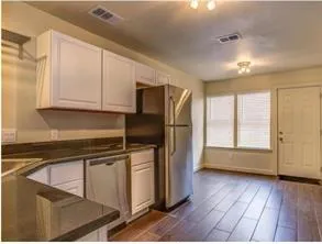 a kitchen with stainless steel appliances granite countertop a refrigerator a sink and white cabinets with wooden floor