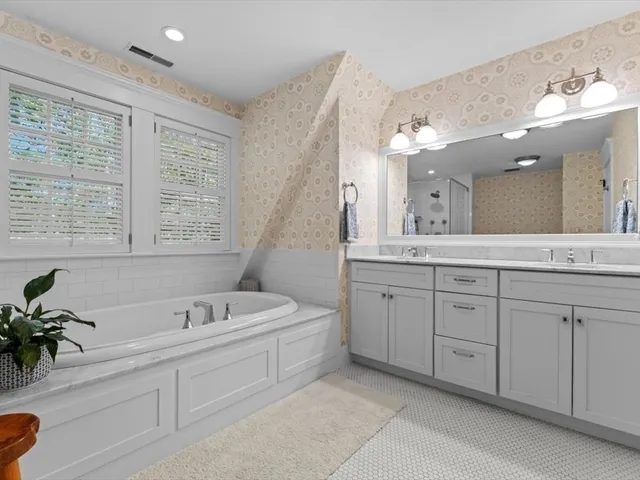 a spacious en suite bathroom with a tub double sink window and mirror