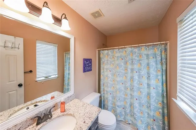 a bathroom with a granite countertop sink toilet a mirror and shower curtain