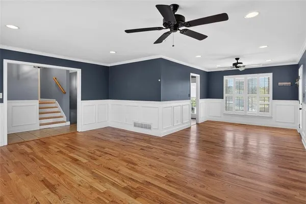 a view of an empty room with wooden floor and a ceiling fan