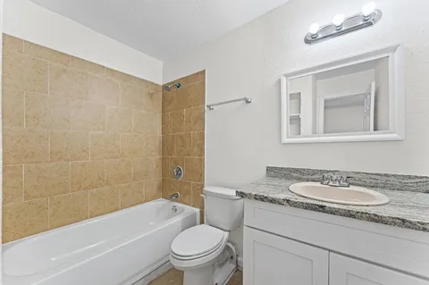 a bathroom with a granite countertop sink a toilet a mirror a bathtub and shower