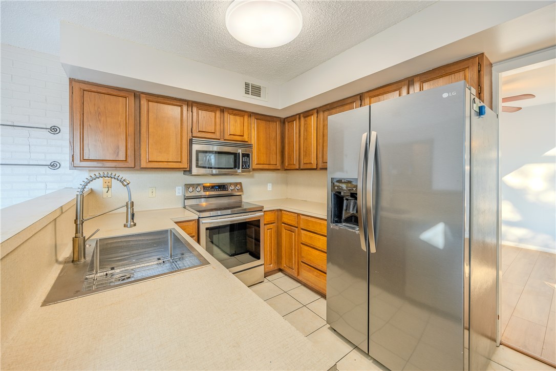 2002 South Lubbock Street Brenham, TX 77833 - Photo 12 of 26 Kitchen with appliances with stainless steel finishes, light countertops, brown cabinetry, light tile patterned floors, and a textured ceiling