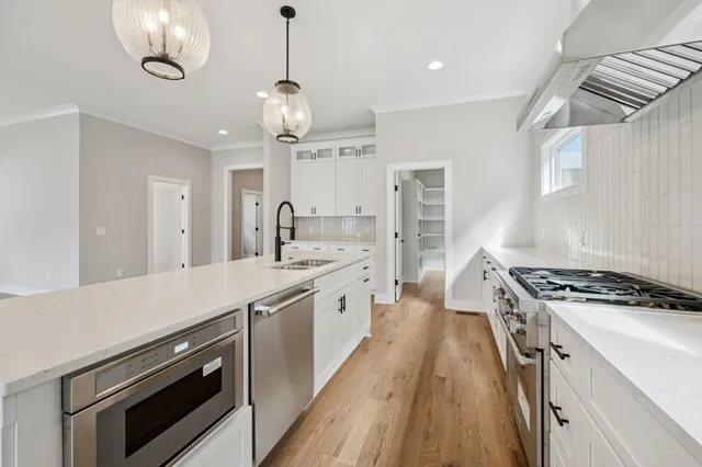 a large kitchen with stainless steel appliances a stove a sink dishwasher and white cabinets with wooden floor