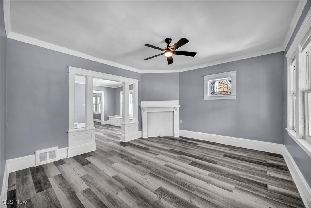 10112 Kinsman Road Cleveland, OH 44104 - Photo 30 of 49 Unfurnished living room with ornamental molding, healthy amount of natural light, wood finished floors, ceiling fan, and decorative columns