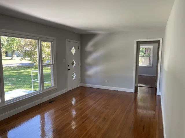 a view of an empty room with wooden floor and a window