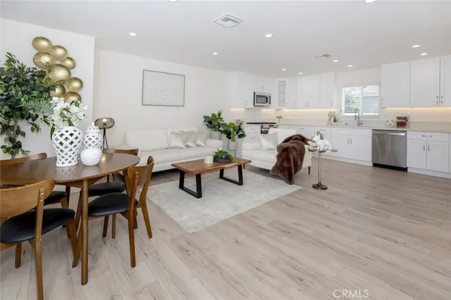 a living room with furniture a dining table wooden floor and kitchen view