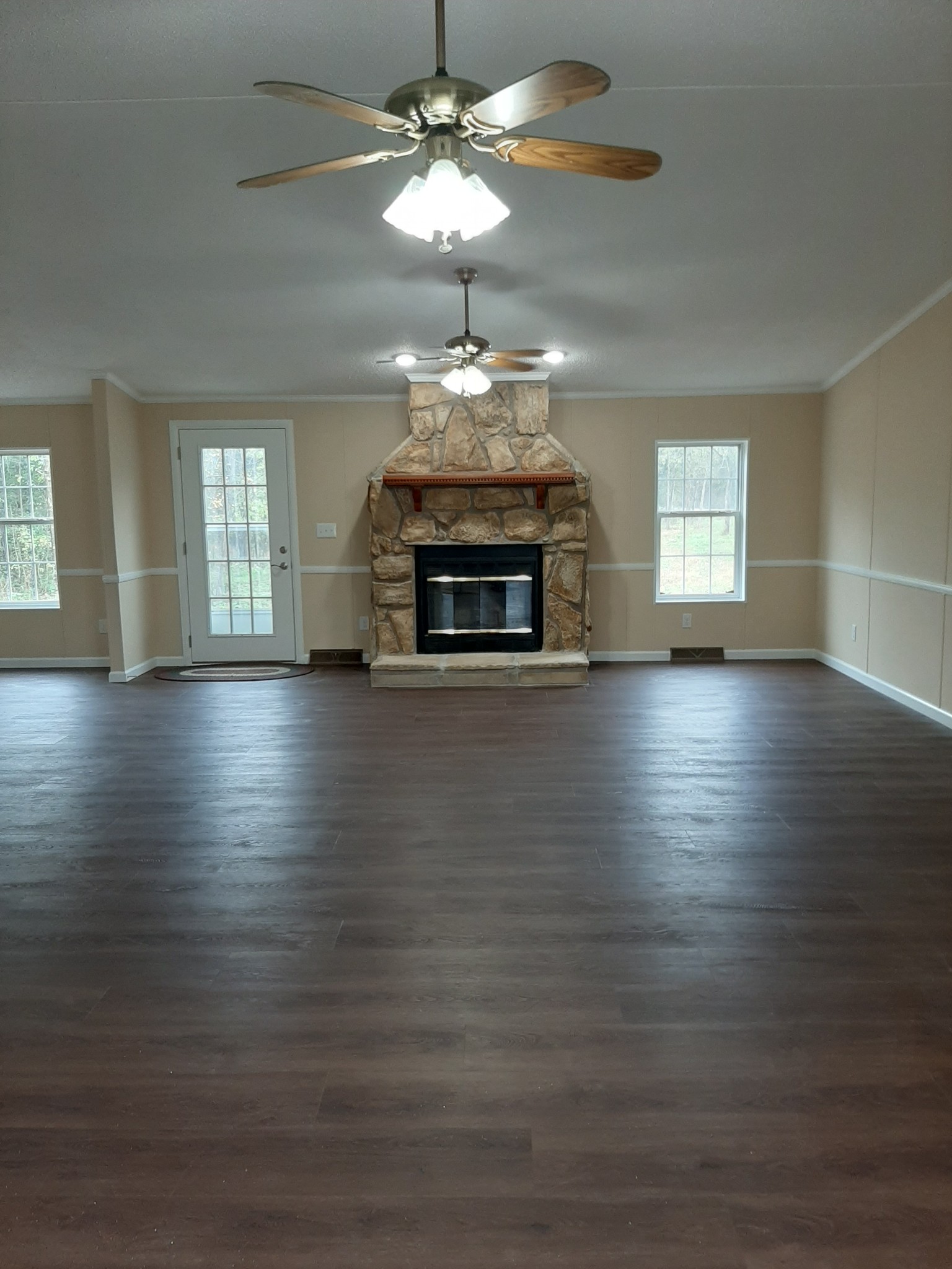 an empty room with wooden floor chandelier fan and fireplace