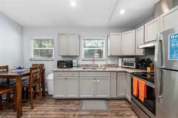 a kitchen with stainless steel appliances granite countertop a stove top oven a sink dishwasher and a refrigerator with wooden floor