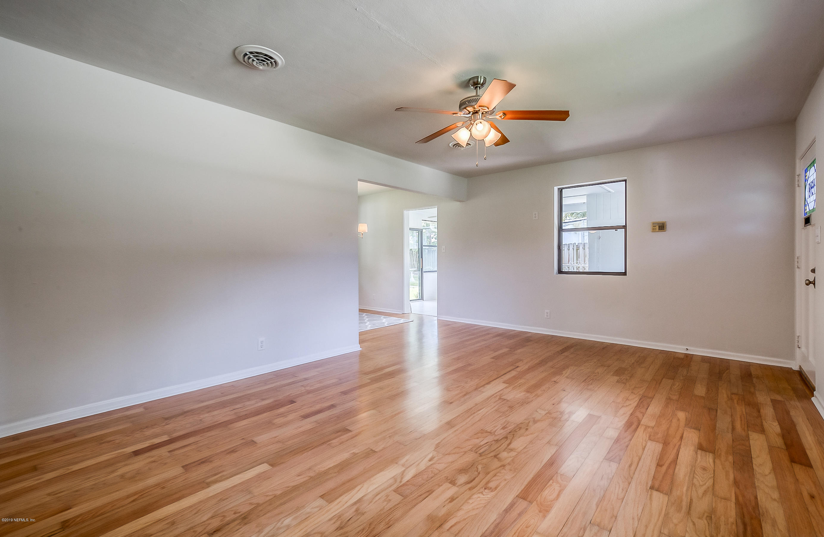 4548 Milstead Road Jacksonville, FL 32210 - Photo 19 of 37 an empty room with wooden floor chandelier fan and windows