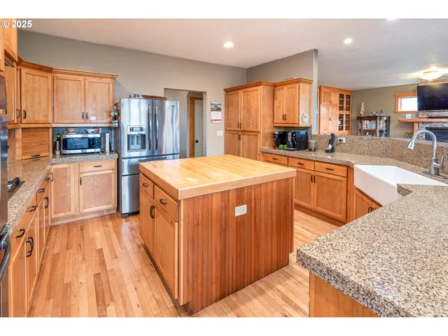 a kitchen with stainless steel appliances kitchen island granite countertop a refrigerator a sink dishwasher and wooden cabinets with wooden floor
