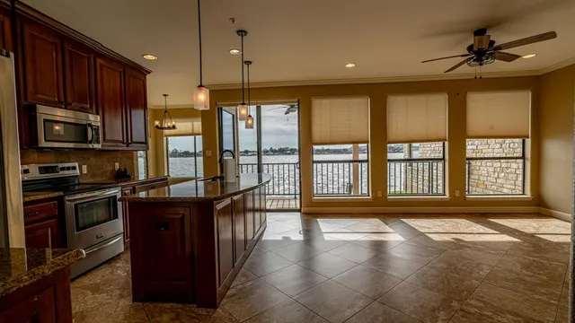 a open kitchen with stainless steel appliances granite countertop a refrigerator a stove and a sink with wooden cabinets