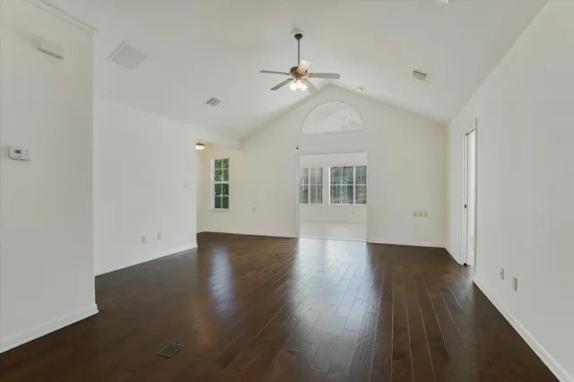an empty room with wooden floor ceiling fan and windows