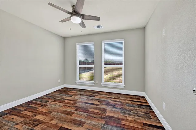 an empty room with wooden floor ceiling fan and window