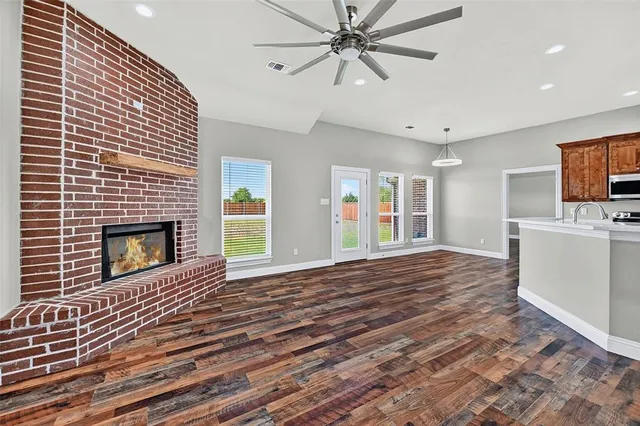 a view of a livingroom with a fireplace a ceiling fan and wooden floor