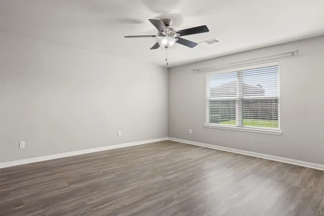 an empty room with wooden floor fan and windows