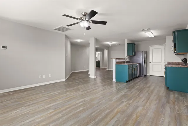 an empty room with wooden floor a ceiling fan a kitchen view and a fireplace