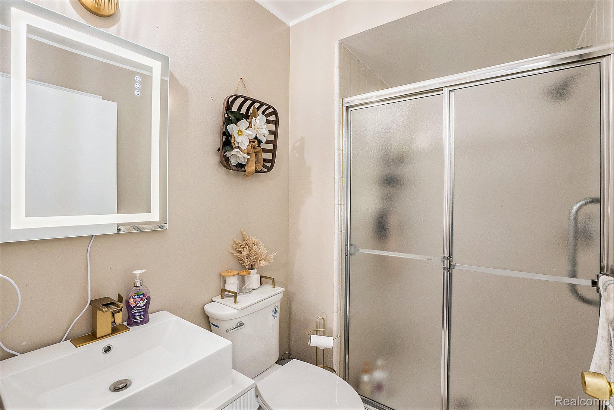 5477 Victory Circle Sterling Heights, MI 48310 - Photo 21 of 32 Bathroom featuring a rectangular vessel sink with a gold-finish faucet, an illuminated mirror, a toilet, and a shower with sliding frosted glass doors