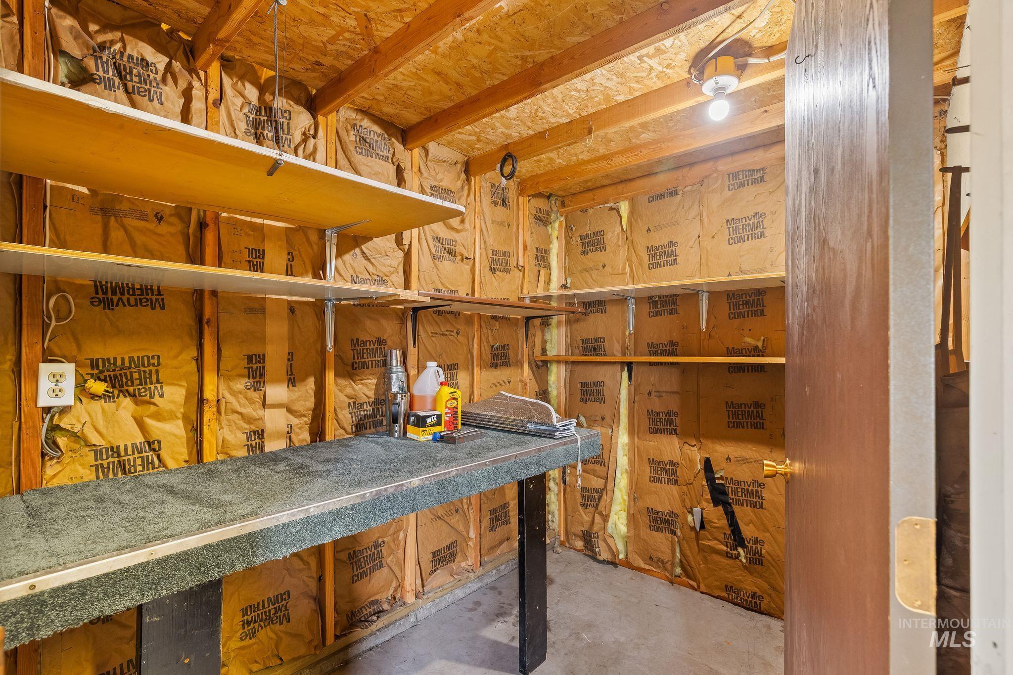 1721 3rd Street Lewiston, ID 83501 - Photo 26 of 45 Utility room featuring open wood shelving, a built-in workbench, exposed insulation, a single light fixture, and a solid-core door