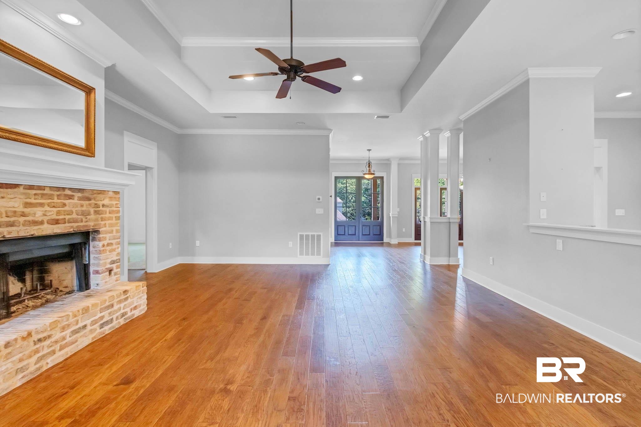 7854 Raegan Lane Daphne, AL 36527 - Photo 11 of 70 Living room with wood finished floors, a brick fireplace, ceiling fan, a tray ceiling, and ornamental molding