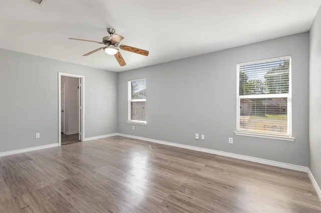 an empty room with wooden floor chandelier fan and windows