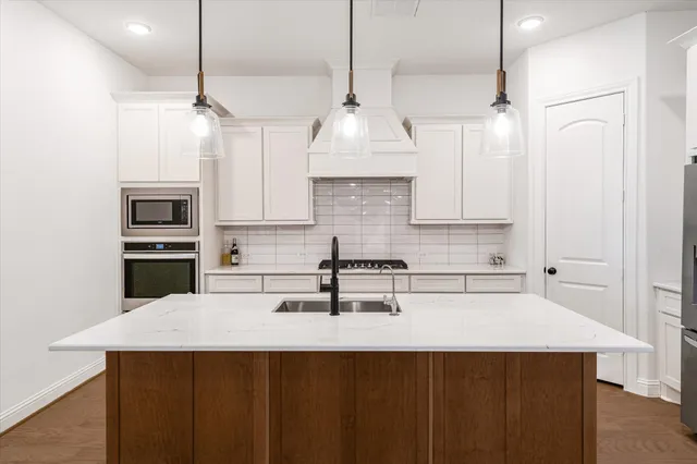 a kitchen with stainless steel appliances a sink a stove a refrigerator and white cabinets with wooden floor