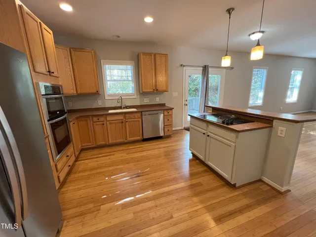 a kitchen with granite countertop a stove a sink a refrigerator wooden floor cabinets and dining table