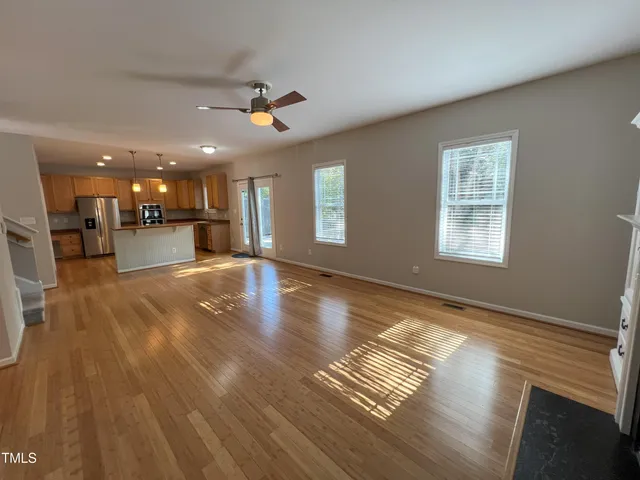 a view of an empty room with wooden floor and a kitchen