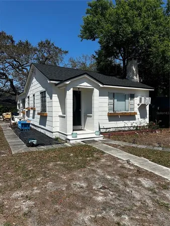 a view of a white house next to a yard with big trees