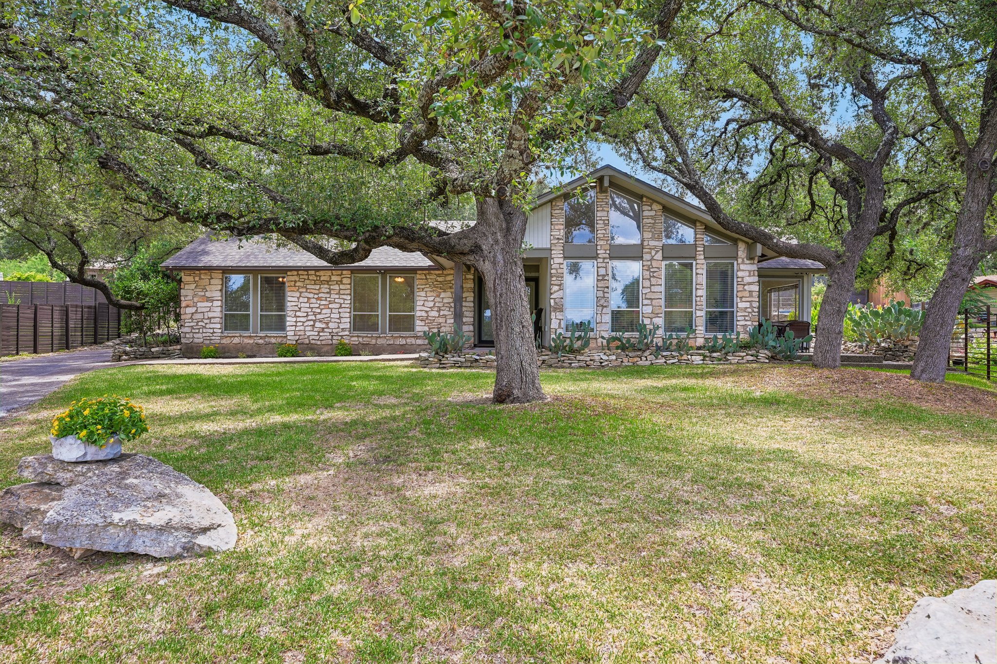 13101 Travis View Loop Austin, TX 78732 - Photo 1 of 27 Mature trees shade this distinctive stone-clad residence, featuring prominent windows and a well-maintained front yard.