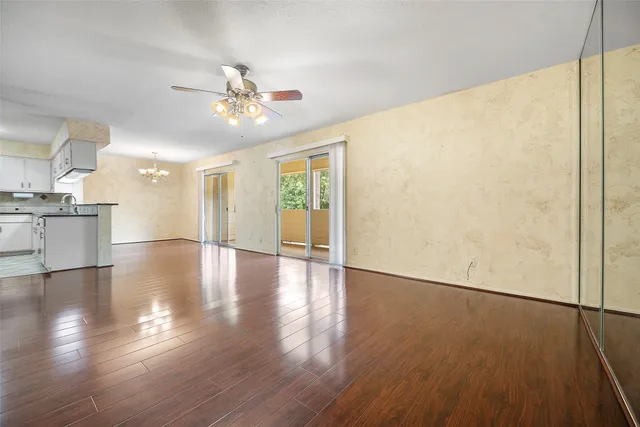 a view of a livingroom with wooden floor a ceiling fan and kitchen space