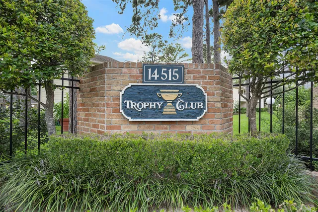 a sign that is sitting on a brick wall with plants and large trees