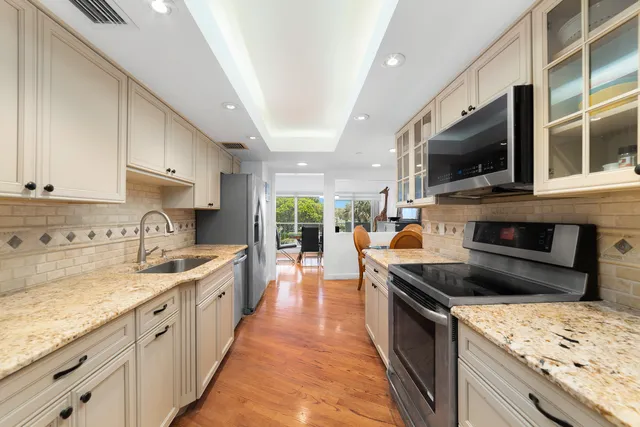 a large kitchen with stainless steel appliances granite countertop a refrigerator a sink dishwasher a stove and white cabinets with wooden floor