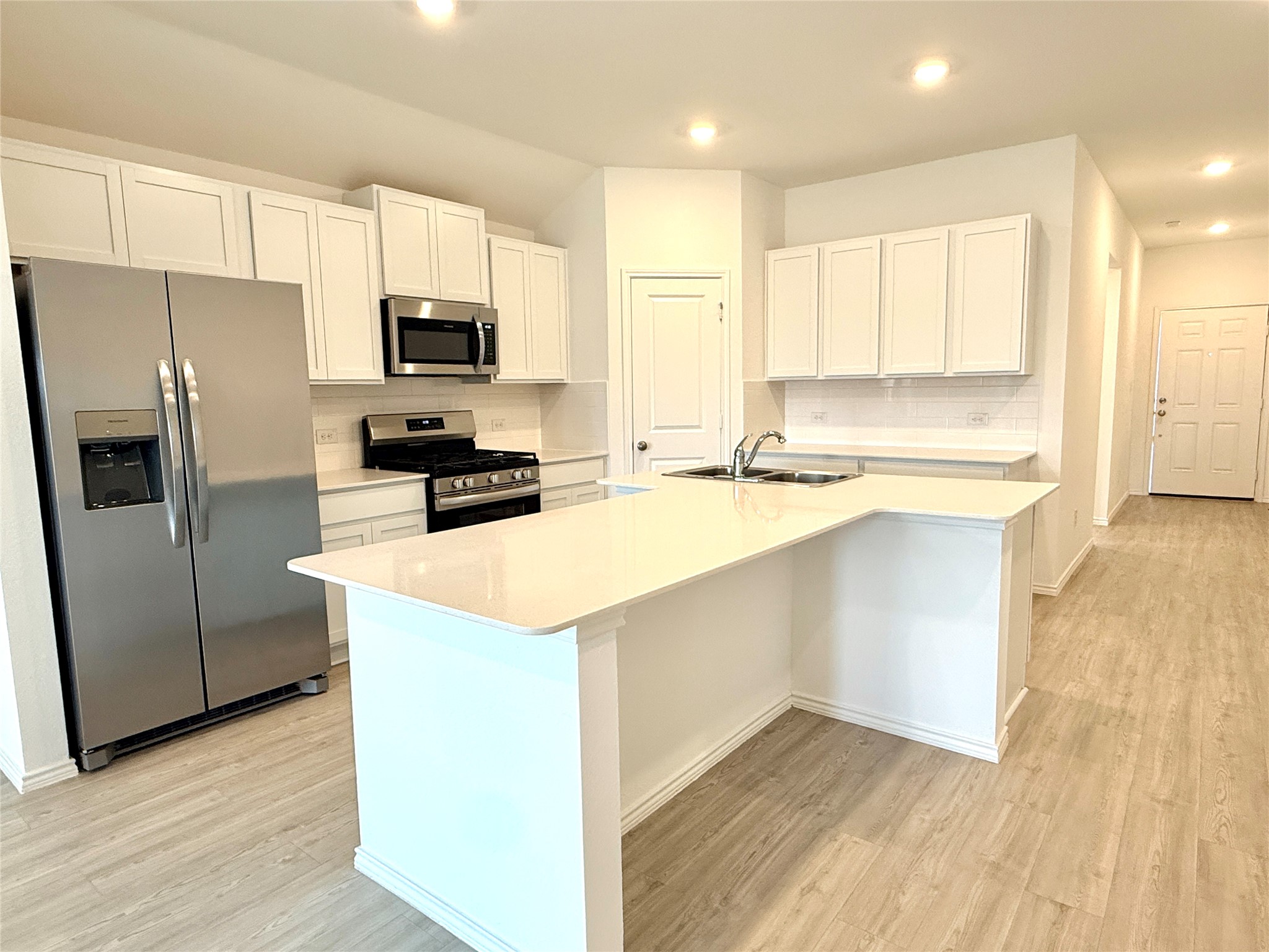 289 Sormonne Loop Kyle, TX 78640 - Photo 10 of 32 Kitchen featuring stainless steel appliances, white cabinets, tasteful backsplash, light wood-style floors, and a kitchen island with sink