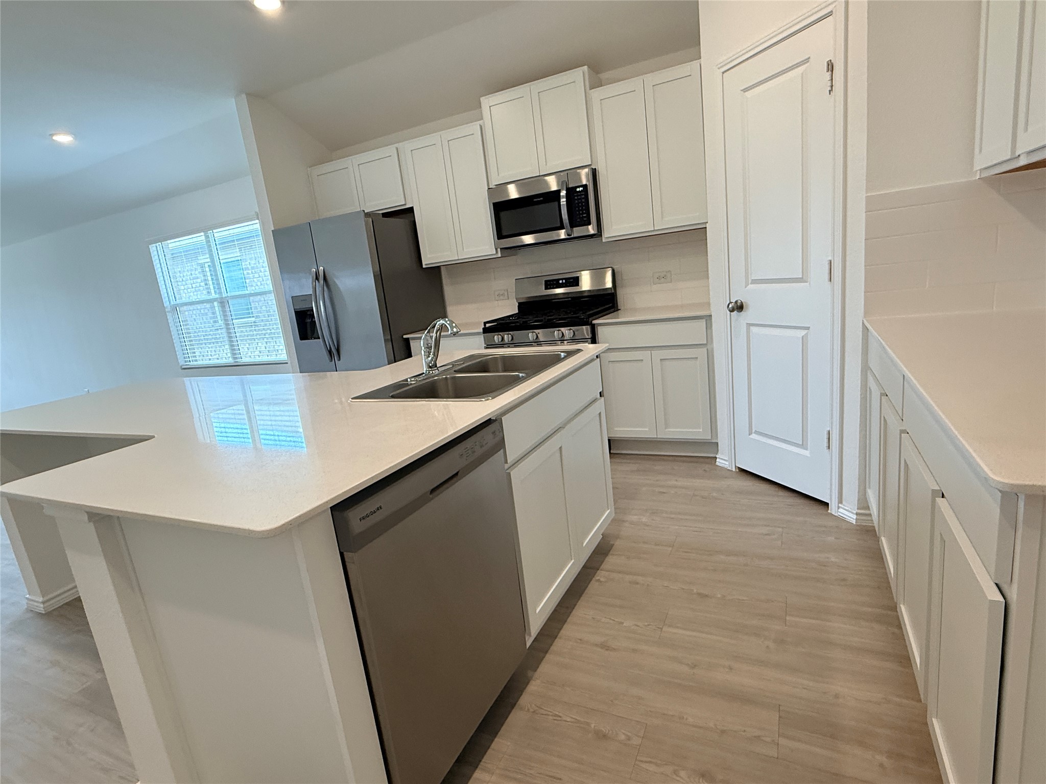 289 Sormonne Loop Kyle, TX 78640 - Photo 18 of 32 Kitchen with an island with sink, white cabinetry, stainless steel appliances, light wood-type flooring, and backsplash
