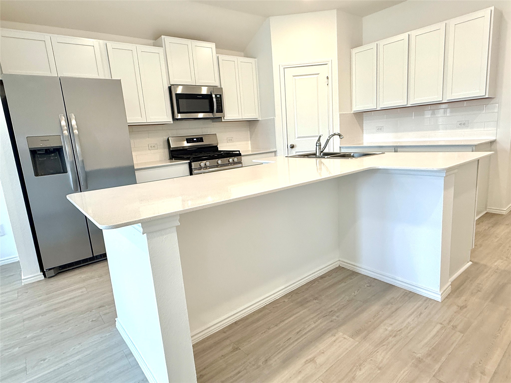 289 Sormonne Loop Kyle, TX 78640 - Photo 19 of 32 Kitchen featuring stainless steel appliances, white cabinetry, light wood-style flooring, a center island with sink, and backsplash