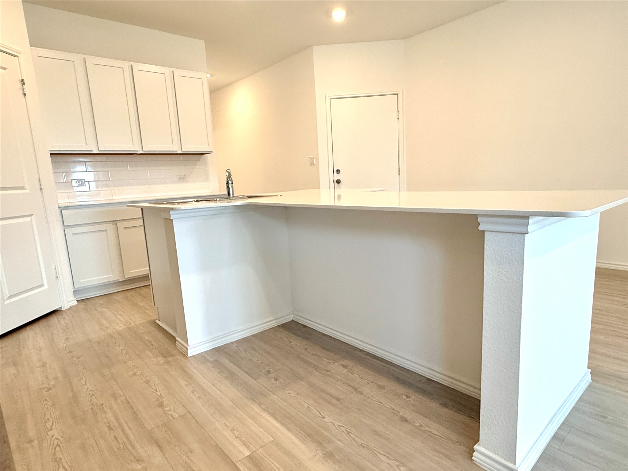289 Sormonne Loop Kyle, TX 78640 - Photo 9 of 32 Kitchen featuring white cabinets, light wood-style flooring, decorative backsplash, a kitchen island with sink, and a breakfast bar area