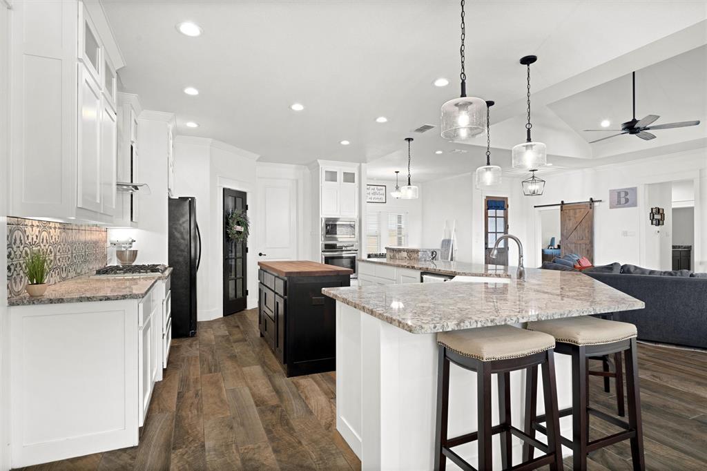 a kitchen with stainless steel appliances kitchen island granite countertop a kitchen island a stove a refrigerator a oven a sink with island and chairs
