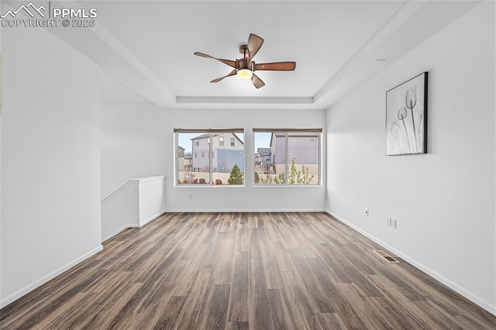 9414 Timberlake Loop Colorado Springs, CO 80927 - Photo 9 of 40 Unfurnished living room featuring two big windows, a raised ceiling, a ceiling fan, and dark luxury vinyl wood finished floors