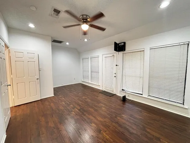 an empty room with wooden floor fan and windows