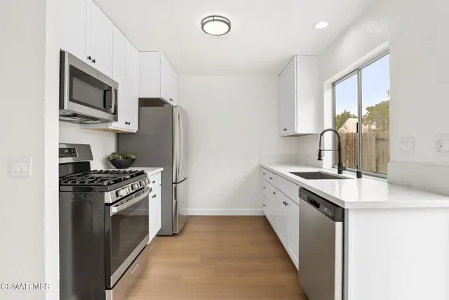 a kitchen with stainless steel appliances granite countertop a stove top oven a sink dishwasher and a refrigerator with wooden floor