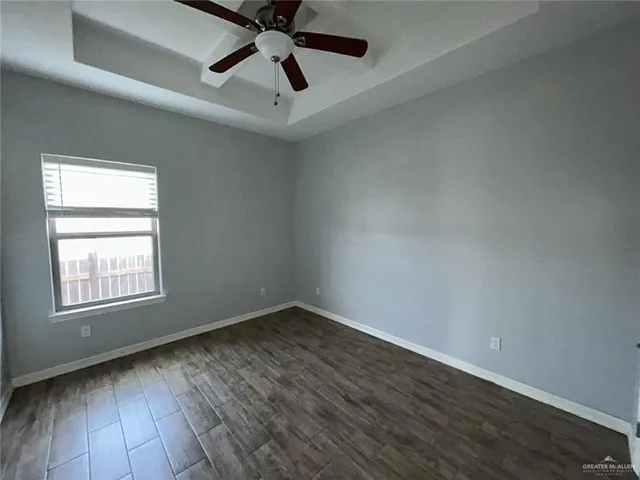 an empty room with wooden floor ceiling fan and windows