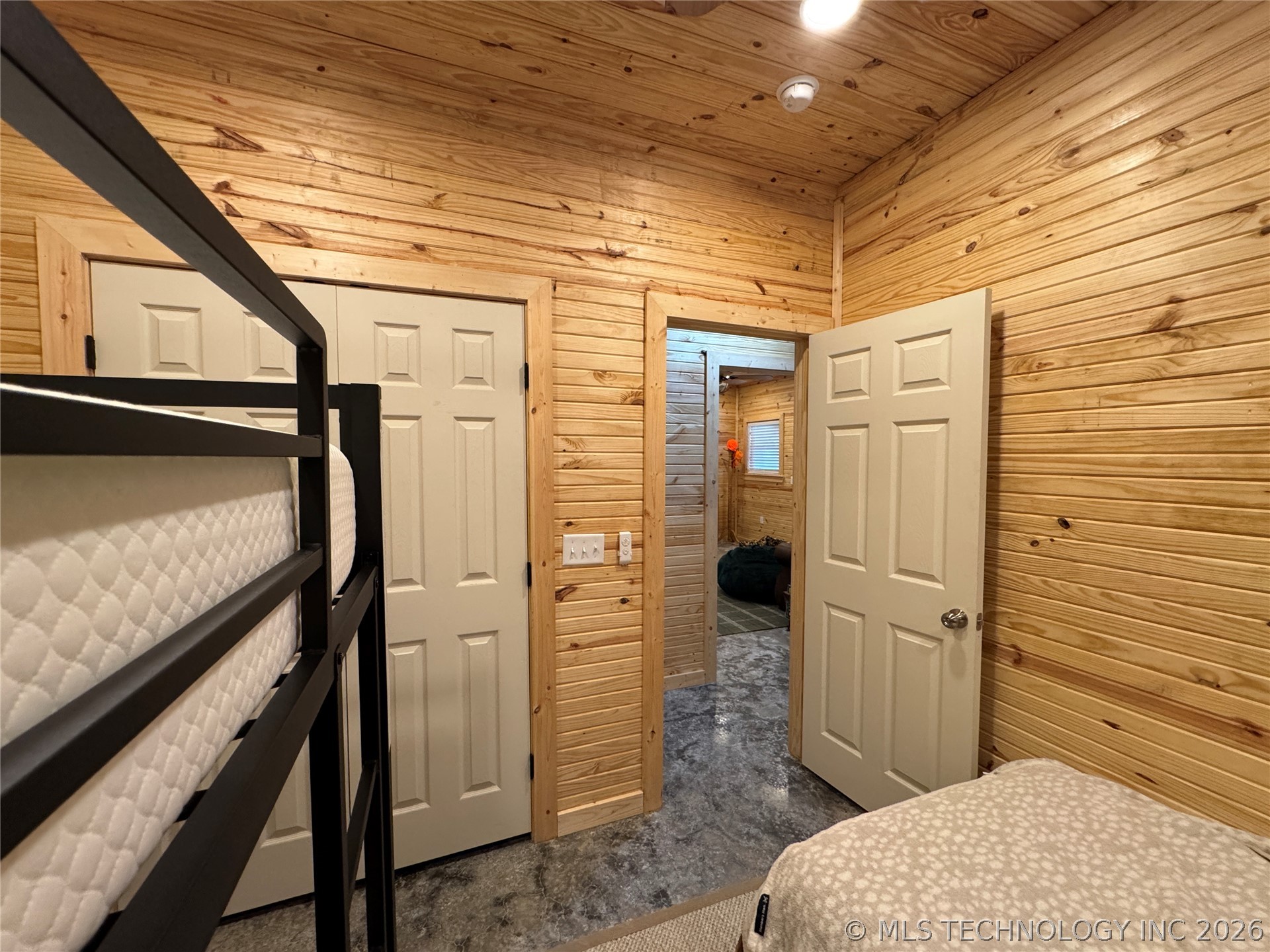 20862 East 1160th Road Keota, OK 74941 - Photo 29 of 47 Wood-paneled room featuring a black metal bunk bed frame, two white paneled doors, and a gray concrete-finish floor