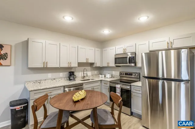 a kitchen with stainless steel appliances granite countertop a refrigerator a sink a stove a dining table and chairs